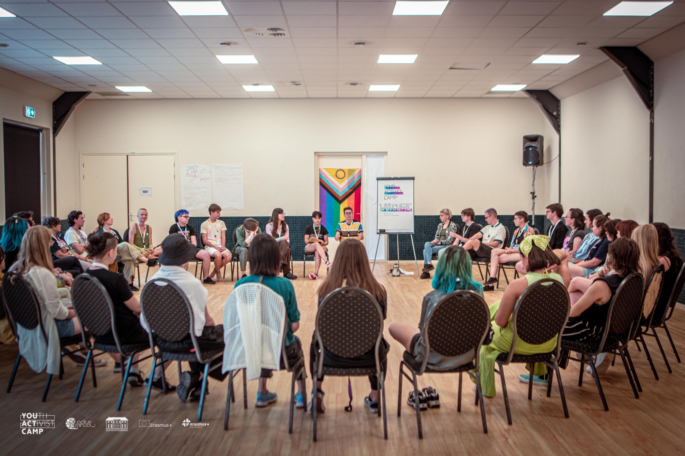 A group of youngsters in a circle, listening to a person leading a workshop.